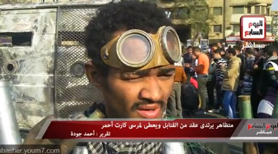 متظاهر يرتدى عقد من القنابل ويعطى لمرسى كارت أحمر