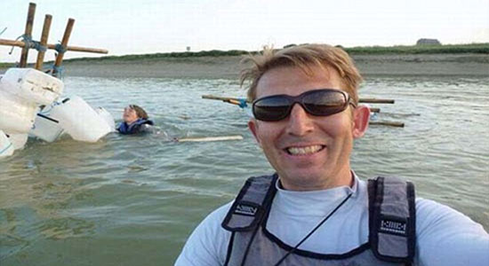 رجل يلتقط صورة سيلفي وهو مبتسم، في حين يصارع آخر في خلفية الصورة للنجاة من الغرق بعدما تحطم به القارب