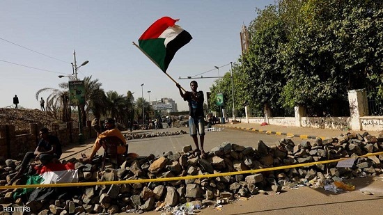 متظاهر سوداني يرفع علم بلاده أمام عوائق أمام موقع الاعتصام.