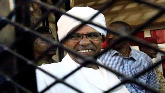 البشير مبتمسا في قفص الاتهام أثناء جلسة محاكمته بقضايا فساد في الخرطوم