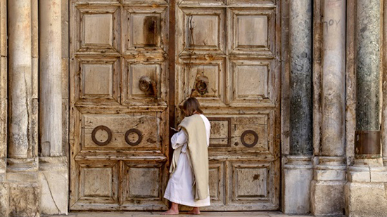 مصلٍ يقف أمام أبواب كنيسة القيامة في البلدة القديمة في القدس الشرقية المحتلة، والمغلقة بسبب تفشي فيروس كورونا المستجد 