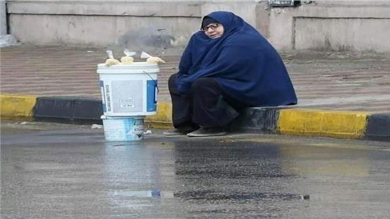 سيدة مسنه تجلس علي الرصيف في عز المطر